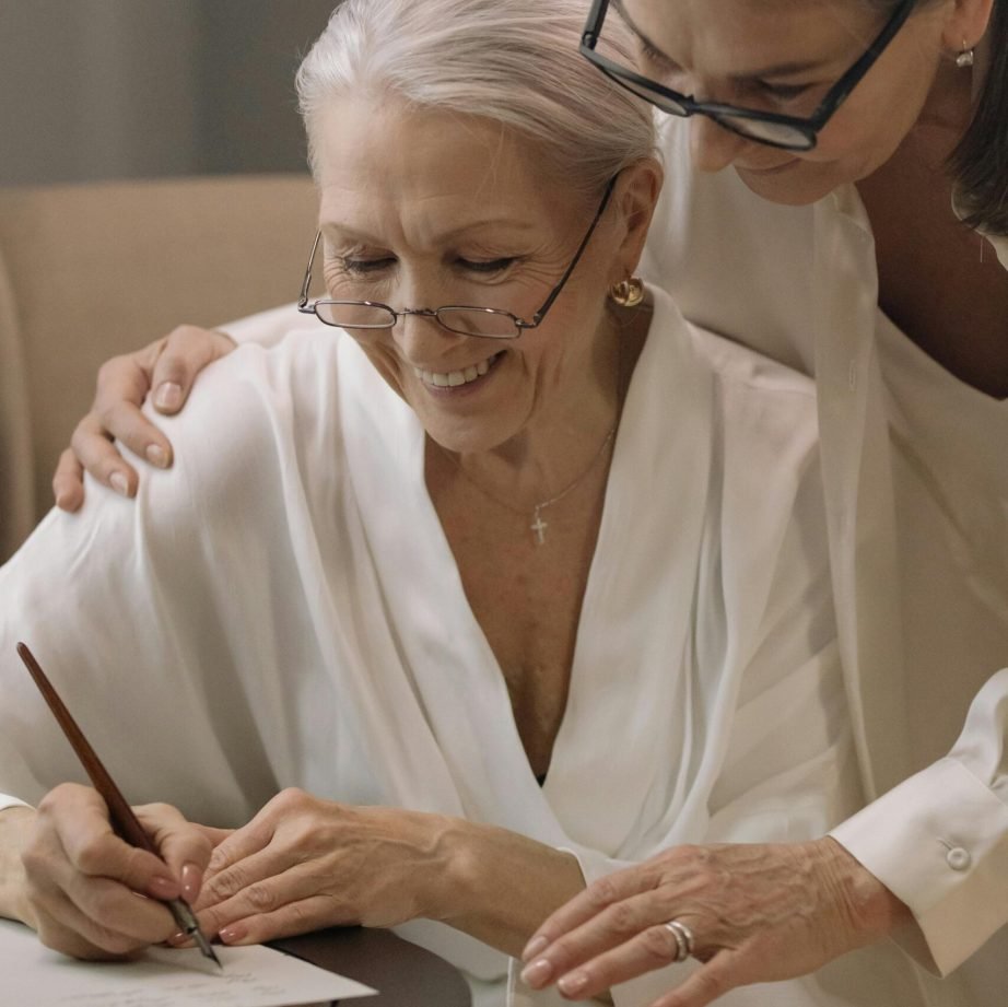 Two senior women sharing a moment of joy and togetherness while writing indoors.